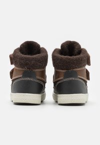 Brune og sorte høje sko med en fluffy brun krave, to justerbare remme og teksturerede hvide gummisåler.
