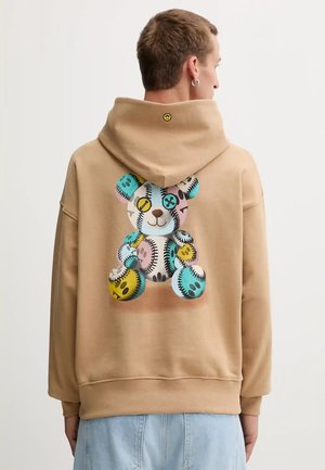 Sudadera con capucha en color marrón claro, con un gráfico colorido de un oso de peluche en la parte posterior, que presenta varios patrones circulares y acentos en colores pastel.