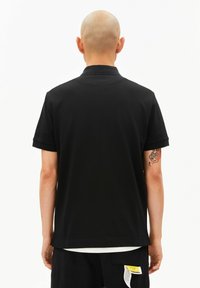 Schwarzes Poloshirt mit kurzen Ärmeln, einem klassischen Kragen und einem geraden Saum. Der Stoff wirkt glatt und leicht. Mit einem Etikett mit Text versehen.