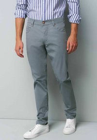Light grey chinos with a slim fit, two front pockets, and a button closure, paired with white sneakers and a blue-striped shirt.