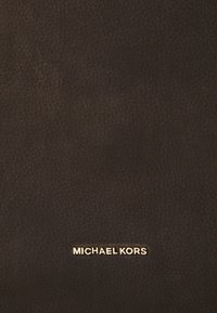 Bruin textuurleer met een gouden "MICHAEL KORS" logo onderaan. Het oppervlak vertoont lichte variaties in textuur.