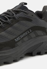 Black hiking shoe featuring a mixed material design with mesh, suede accents, and a patterned upper. Notable logo placement on the side.