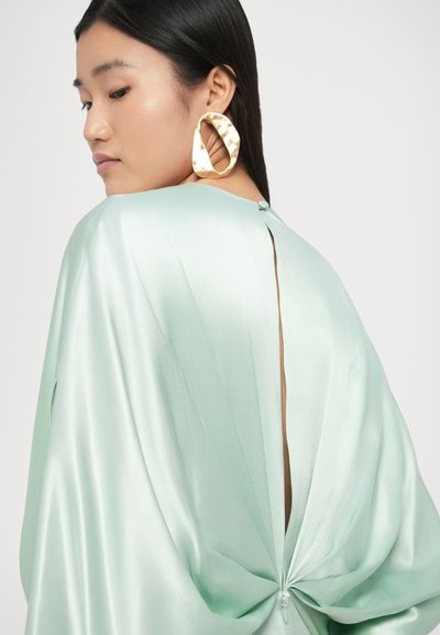 Τοπ από σατέν σε μέντα πράσινο με ντραπέ σχέδιο, διαθέτει άνοιγμα στην πλάτη και κούμπωμα με κουμπιά, συνδυασμένο με μεγάλα χρυσά σκουλαρίκια κρίκους με υφή.