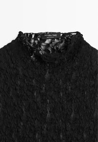 Schwarzes Spitzentop mit hohem Kragen und filigranem Muster. Das Etikett trägt die Aufschrift "Massimo Dutti" mit Pflegehinweisen. Leichter, strukturierter Stoff.