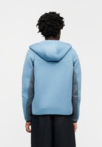 Ανοιχτό μπλε φούτερ με γκρι λεπτομέρειες, υφή ύφασματος, φαρδιά κουκούλα και επιμηκυμένη πίσω όψη. Διαθέτει άνετη εφαρμογή και ραφές σχεδιασμένες με προσοχή.