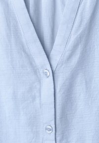 Tissu bleu clair texturé avec un col en V et deux boutons blancs le long de l'ouverture avant d'un vêtement.