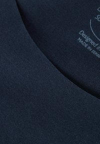 Marinblått bomullstyg med en slät textur och rundad halsringning; har tryckt text som anger design- och tillverkningsdetaljer.