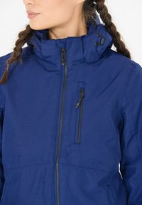 Marineblaue Kapuzenjacke mit Reißverschluss vorne, strukturiertem Stoff und einer Brusttasche. Verfügt über verstellbare Kordeln an der Kapuze.