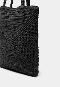 Černá tkaná taška přes rameno s texturovaným vzorem, s pletenými rukojeťmi; vyrobena z odolného materiálu, nabízí prostorný interiér pro uložení.