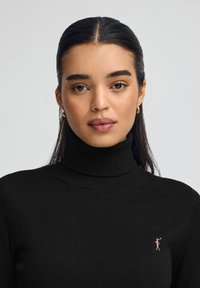 Czarny golf z miękkiej dzianiny o dopasowanym kroju. Posiada małe haftowane logo na lewej piersi.