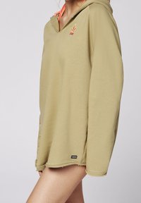 Sweat à capuche vert olive à coupe décontractée, avec un petit logo coloré, des coutures apparentes et un ourlet incurvé.