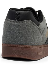 Szare zamszowe sneakersy z czarnym skórzanym obcasem i brązową gumową podeszwą, charakteryzujące się teksturowanym wykończeniem oraz trójkątnymi akcentami na podeszwie.