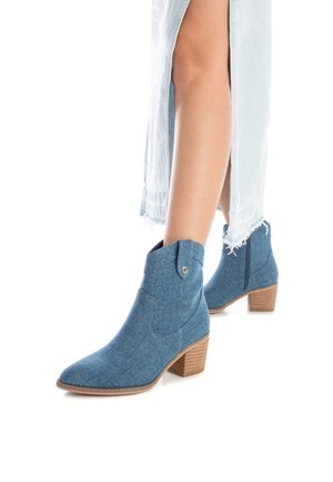 Stivaletti in denim con punta affusolata, di colore blu chiaro, cuciture decorative e tacco in legno impilato. Presenta un dettaglio con bottone a pressione.