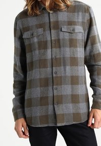 Flanellhemd im grauen und olivgrünen Karomuster, mit knöpfbarem Frontbereich, zwei Brusttaschen und langen Ärmeln. Strukturierten Stoff.