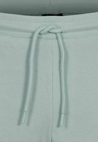 Ljusgröna, texturerade sweatpants med dragsko i midjan. Har en ribbad yta och kontrasterande snörspetsar. Enkel design utan utsmyckningar.