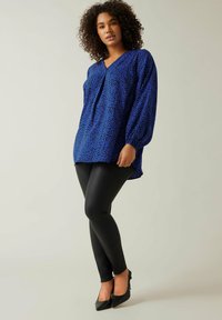 Blusa blu con stampa leopardo, scollatura a V e maniche a palloncino, abbinata a leggins neri e tacchi a punta neri. Tessuto liscio in tutta la lunghezza.