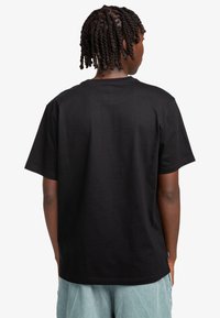 Black cotton t-shirt with a crew neck, short sleeves, and a relaxed fit. Features visible stitching and a tag at the hem.