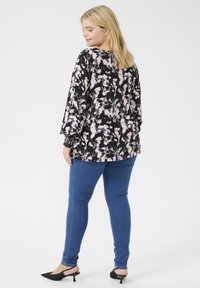 Mönstrad blus i svart, rosa och kräm, med långa ärmar och elastiska manschetter. Kombinerad med blå slim-fit jeans och svarta klackmules.