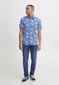 Blå kortermet skjorte med hvite sirkulære mønstre; knappes opp-stil med krage; kombinert med mørkeblå slim-fit jeans og svarte sneakers.