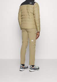 Veste beige isolée avec panneau d'épaule noir, associée à un pantalon cargo beige. Chaussures avec des accents gris, noir et orange.