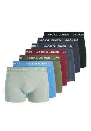 Jeune homme aux cheveux bouclés portant un boxer Jack & Jones gris clair, debout devant un fond blanc uni.