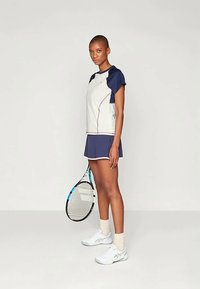 Tenisa tērps ar baltu un tumši zilu augšu, tumši zilu svārku un baltām kurpēm. Iekļauta tenisa nūja ar zilu akcentu. Īso piedurkņu dizains.