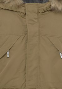 Close-up of tan winter coat front with vertical zipper covered by fabric flap and fur-lined hood at top.