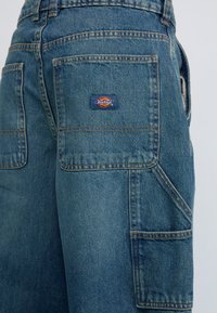 Blaue Denim-Cargo-Shorts mit mehreren Taschen, kontrastierenden Nähten und einem Dickies-Logo-Patch auf der hinteren Tasche.