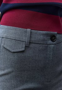 Gros plan sur un pantalon gris ajusté avec rabat de poche latérale et bouton noir, assorti à une chemise rayée bleu marine et bordeaux.
