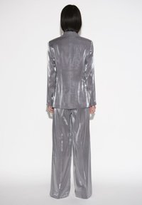 Zilveren glanzend pak met een getailleerde blazer en wijde broekspijpen, met een gladde textuur en strak ontwerp, gezien vanaf de achterkant.