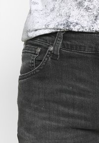 Svarta denimjeans med en strukturerad yta, utrustade med framp fickor och metalldetaljer. Passformen är kroppsnära.