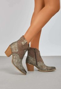 Bottines en daim vertes avec un embout arrondi, des coutures décoratives, une fermeture éclair sur le côté et un talon en bois empilé.