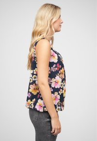 Virágmintás, kék háttérrel rendelkező tank top, színes virágokkal. Az anyag könnyű, laza fazonú és kerekített aljú.