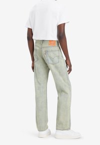 Jeans de mezclilla verde claro con un corte relajado, cinco bolsillos y una etiqueta de cuero en la cinturilla. Llevados con una camiseta blanca y zapatos blancos.