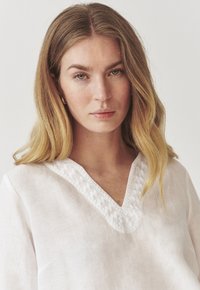 Balta lina blūze ar V-veida izgriezumu un teksturētu izšuvumu ap kakla izgriezumu. Mīksts, viegls audums ar brīvu piegriezumu.