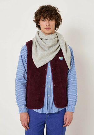 Gilet in pile bordeaux con bottoni a pressione, indossato sopra una camicia a righe blu, abbinato a una sciarpa triangolare grigio chiaro. Dettagli di design minimalisti.