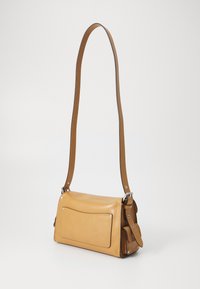 Tan leather crossbody bag with a flat rectangular shape, short shoulder strap, and a front pocket featuring silver hardware accents.