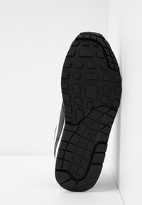 Semelle de sneaker noire avec un motif de grip texturé, dotée de crampons profonds pour une traction et d'un accent latéral blanc contrastant.