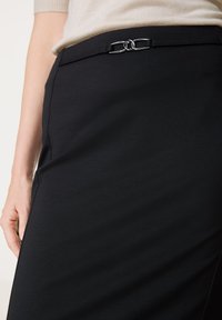 Schwarzer Bleistiftrock aus einem weichen Stoff. Verfügt über ein schlankes Design mit silbernen Kettenakzenten am Taillenbund.