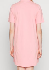 Robe polo rose à manches courtes, en tissu doux, coupe droite, et col. Pas de motifs ni d'accents visibles.