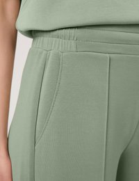Light green, stretchy fabric pants with an elastic waistband, side pockets, and stitched pleats for added texture and design detail.