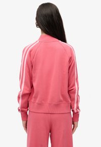 Sudadera rosa con cuello acanalado, mangas largas y rayas laterales blancas a contraste. Textura suave, ajuste relajado y cintura elástica.