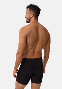 Calzoncillos boxer negros con una cinturilla roja, que presentan un ajuste ceñido y una textura suave. Mostrados en un modelo masculino de espaldas.