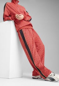 Chándal rojo hecho de un tejido texturizado, con un diseño estampado, rayas laterales en contraste y una chaqueta con cremallera y cuello alto.
