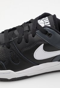 Sapatilha de couro preta com um logo swoosh branco, detalhes texturizados e atacadores pretos. A sola é branca com uma parte inferior de borracha preta.
