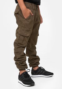 Kaki cargo-bukser med elastiske manchetter og sidelommer; kombinert med svarte joggesko med tre striper og hvit såle.