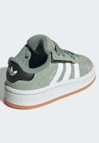 Zelené semišové tenisky s bílými pruhy, černým akcentem na patě, gumovou podrážkou a texturovanými tkaničkami.