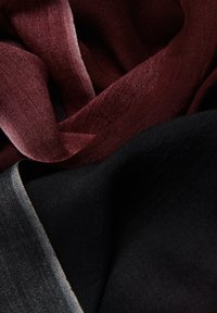 Deux tissus qui se chevauchent : un bordeaux profond et un noir uni. Les deux ont une texture douce et lisse avec un léger éclat, mettant en valeur leur apparence luxueuse.