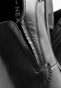 Schwarzer Lederschuh mit einem schlanken Design, sichtbaren Nähten und dezenten Falten, die die Textur und Verarbeitung des Materials hervorheben.