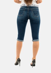 Jeans capri in denim blu scuro con orli arrotolati, dotati di due tasche posteriori e un design cucito sottile. Abbinati a tacchi alti neri.